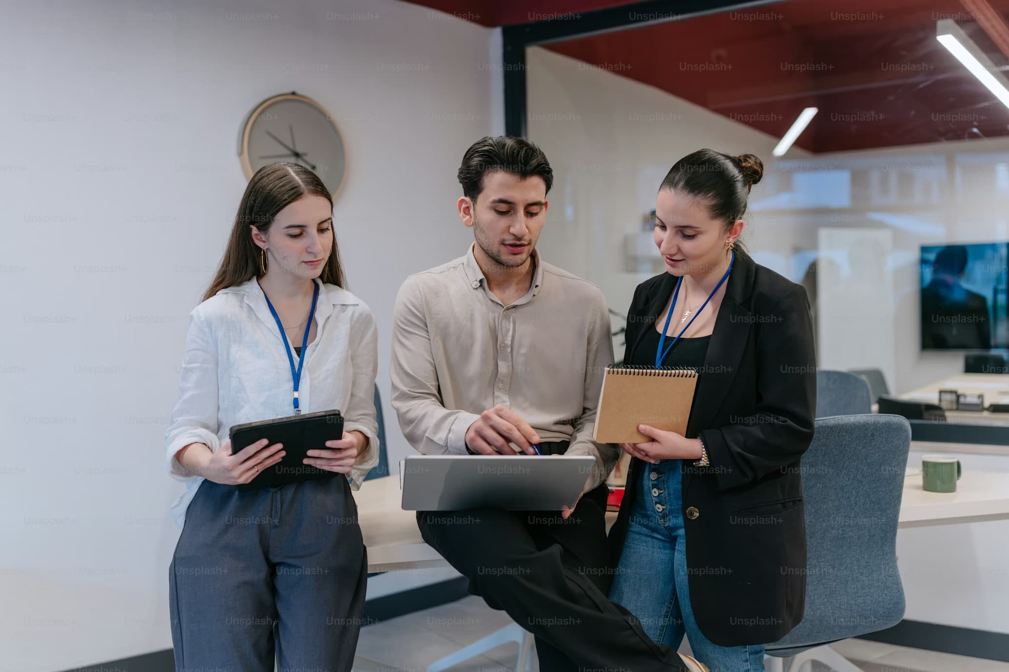 Three young professionals collaborating around a laptop and tablet in a modern office setting.