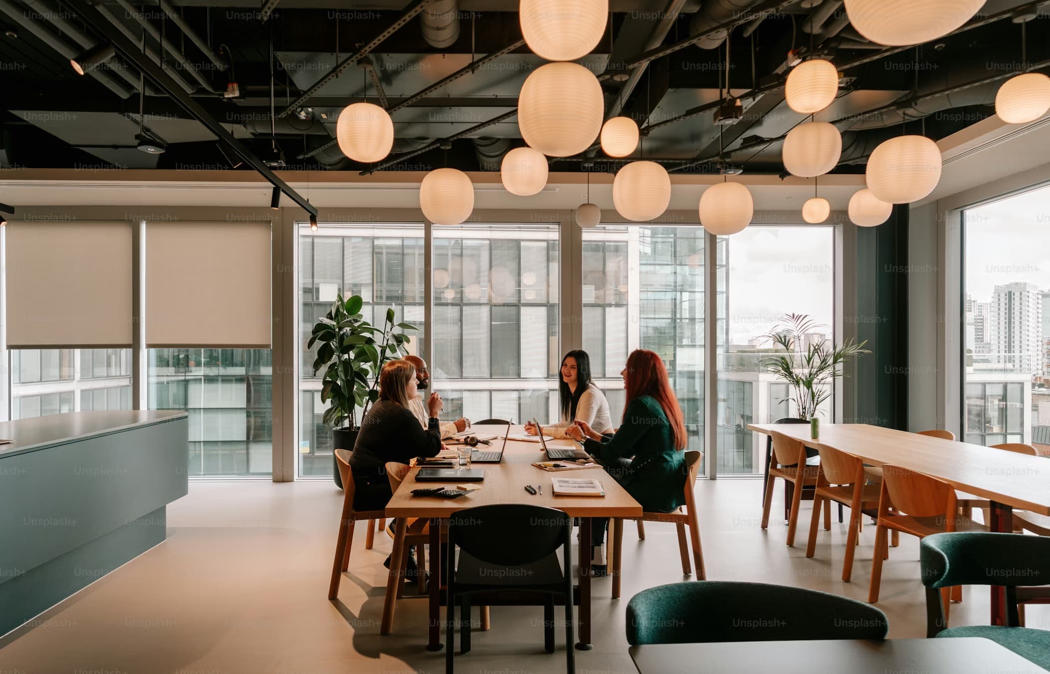 Four professionals collaborating at a wooden table in a modern office with paper lanterns.